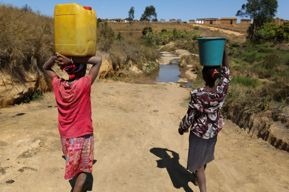 Fara (red shirt) and her older sister on their way back home with a bucket and jerrycan full of dirty water on their heads in Fenoarivo village, Madagascar. On average, girls spend around six hours a day collecting water. This is a familiar image across the rest of the country, where nearly half of the population lives without access to safe water and a decent toilet.Photo credit: WaterAid/ Ernest Randriarimalala